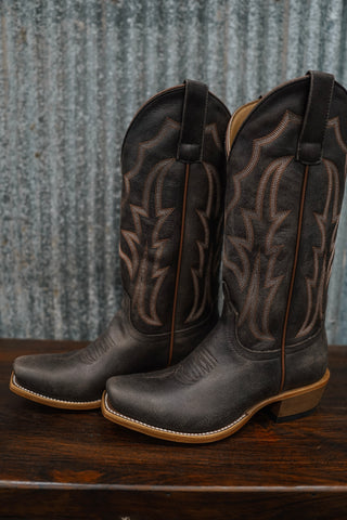 Pair of dark brown leather cowboy boots on a wooden surface with a rustic metal background.