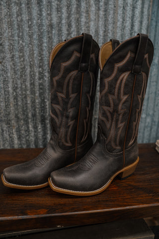 Pair of black cowboy boots with brown leather trim on a wooden surface.
