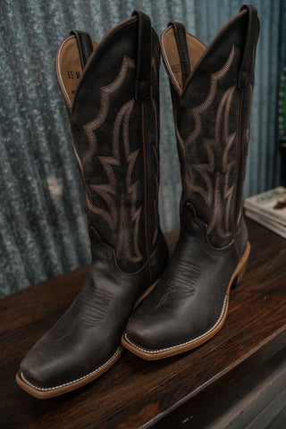 Pair of black cowboy boots with intricate designs on a wooden surface.