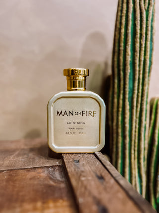 Perfume bottle labeled 'Man on Fire' on a wooden surface with a cactus in the background