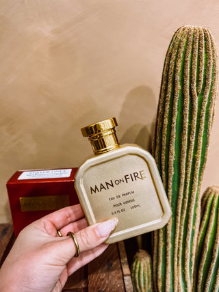 Gold 'Man on Fire' perfume bottle held by a hand with a cactus in the background