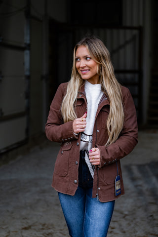 Woman wearing a brown jacket with a visible brand label, standing in an indoor setting.