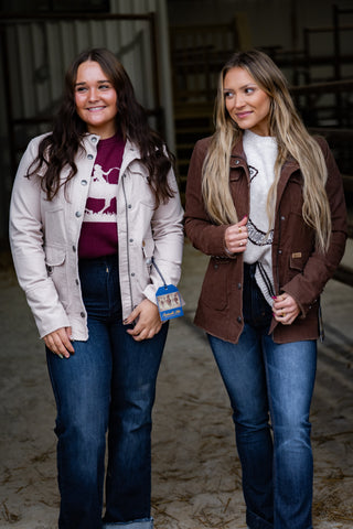 Two women standing side by side in a barn setting, wearing jackets and jeans.