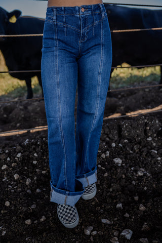 Person wearing blue jeans standing in a field with a cow in the background