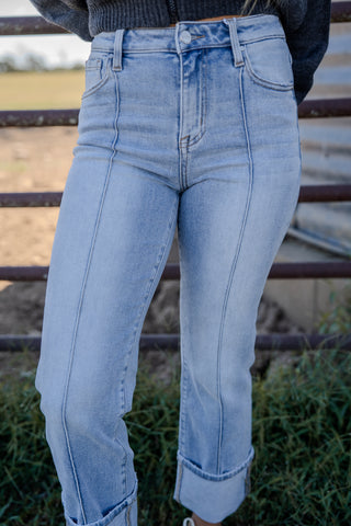 Light blue jeans worn by a person standing outdoors with a metal railing and grass in the background.