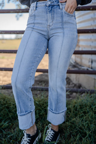 Person wearing light blue jeans standing in front of a metal fence.
