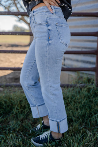 Person wearing light blue jeans standing in a grassy area with a wooden fence in the background.