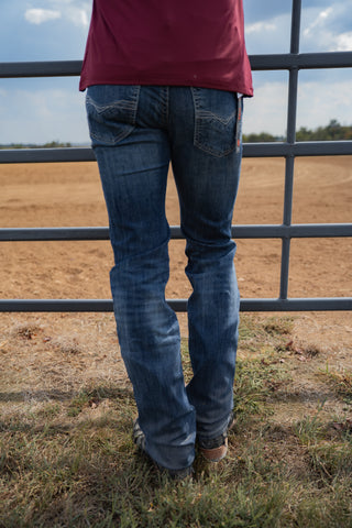 Person wearing blue jeans standing in front of a metal fence with a field in the background