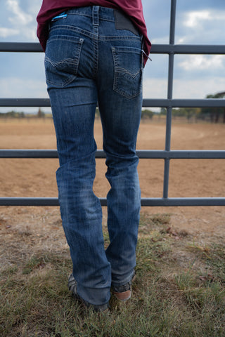 Person wearing blue jeans standing in front of a metal fence with a field and sky in the background