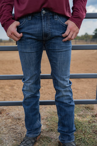 Person wearing blue jeans standing in a field with a fence in the background