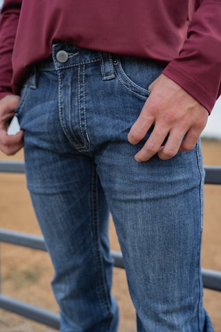 Person wearing blue jeans and a maroon long-sleeve shirt standing near a metal fence.