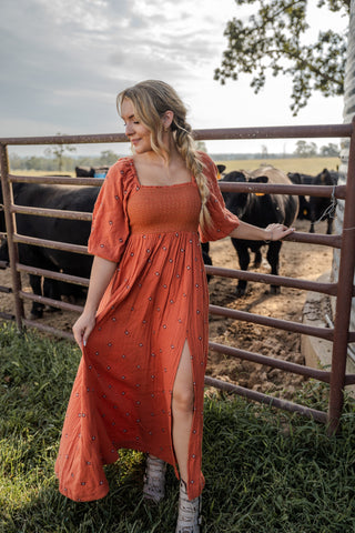 Woman in an orange dress standing in a fenced area with cows.