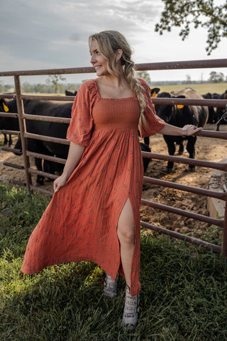 Woman in a red dress standing next to a fence with cows in the background