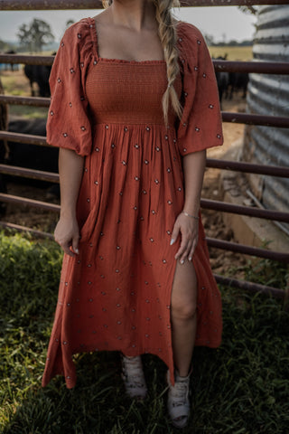 Woman wearing a rust-colored dress with embellishments in an outdoor setting.