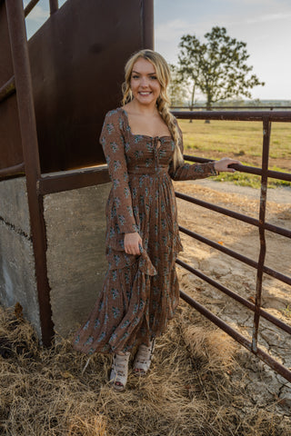 Woman in a long dress standing next to a metal gate with a field and tree in the background