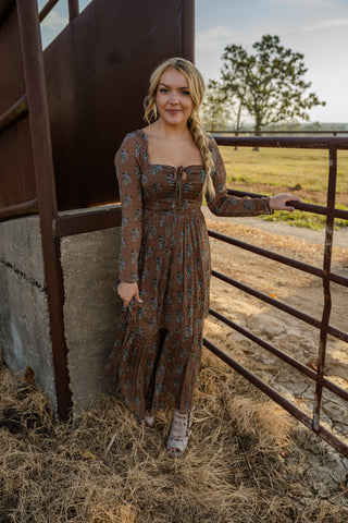 Woman in a long dress standing next to a metal gate in a rural setting
