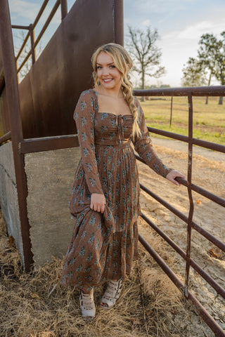 Woman in a patterned dress standing next to a metal gate in an outdoor setting
