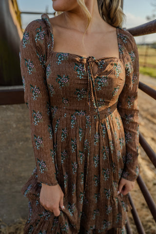 Woman wearing a brown floral dress standing outdoors.