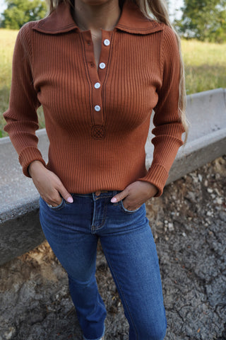 Person wearing a brown ribbed sweater and blue jeans standing outdoors.
