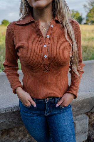 Woman wearing a brown ribbed sweater and blue jeans with a blurred natural background