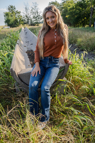 Woman sitting on a concrete bench in a grassy field with trees in the background