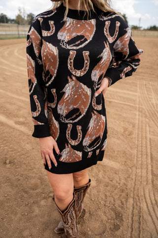 Person wearing a black dress with horse and horseshoe pattern outdoors on a dirt surface