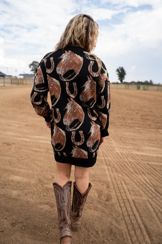 Person wearing a patterned jacket and cowboy boots on a dirt field