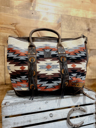 Patterned leather bag with brown handle on a wooden surface
