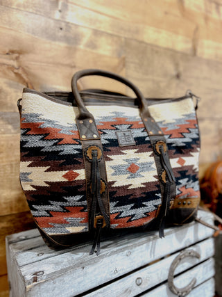 Patterned handbag with leather accents on a wooden surface