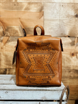 Brown leather backpack with intricate patterns on a wooden surface