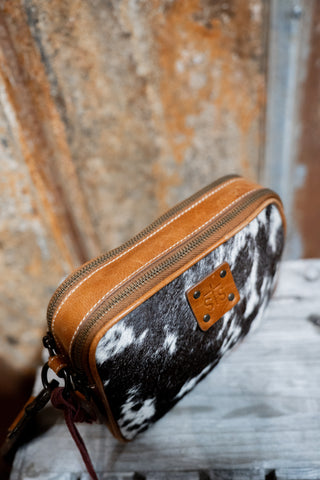 Cowhide leather pouch with brown zipper and leather tag on a textured surface