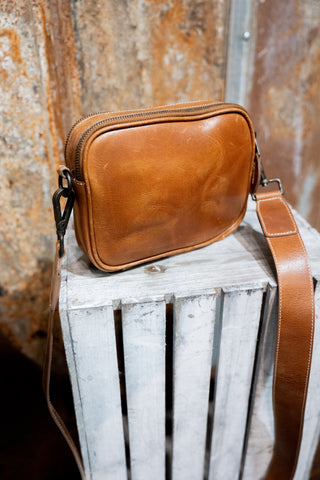 Brown leather crossbody bag on a rustic wooden surface