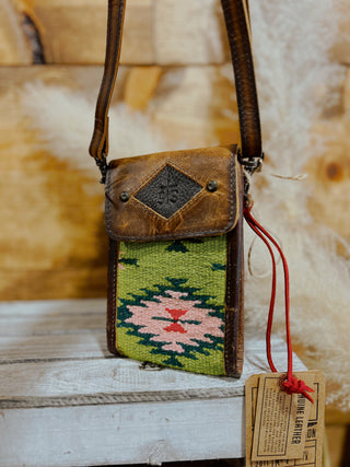 Small leather crossbody bag with embroidered green panel on a wooden surface