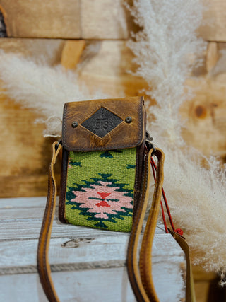 Small crossbody bag with a green patterned front panel on a wooden surface.
