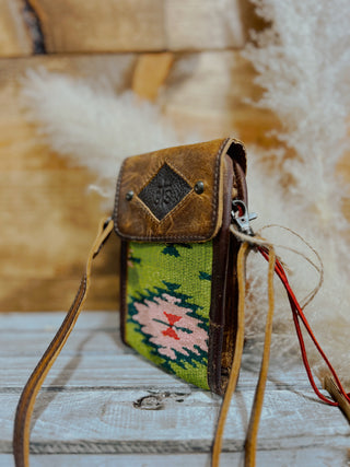 Small leather crossbody bag with a green patterned flap on a wooden surface.