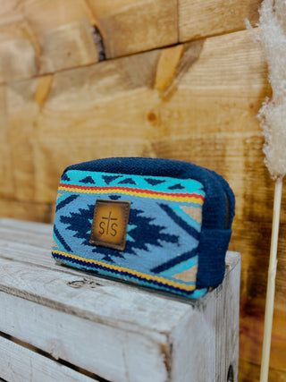 Blue and teal patterned pouch with a brand logo on a wooden surface