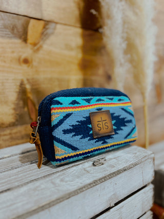 Blue and multicolored patterned pouch with 'sts' logo on a wooden surface