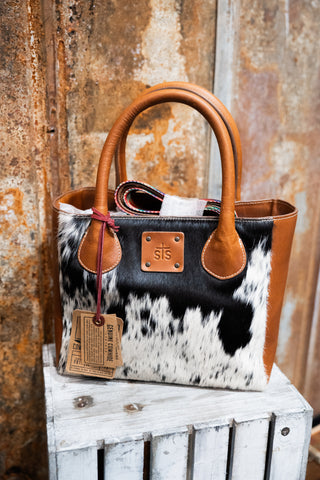 Handbag with cow print and brown leather accents on a wooden surface