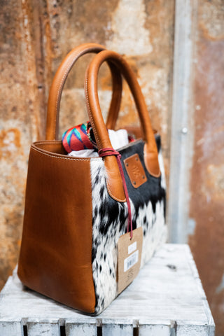 Brown leather handbag with cowhide pattern on a wooden surface
