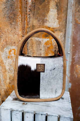 Handbag with cowhide pattern and visible brand logo against a rusty metal background