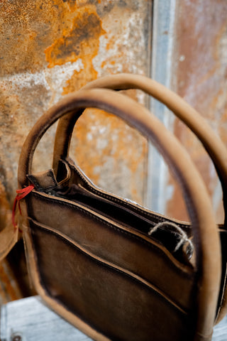 Brown leather handbag with a worn handle against a rusty metal background