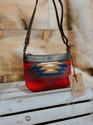 Red and blue patterned handbag with a tag on a wooden surface