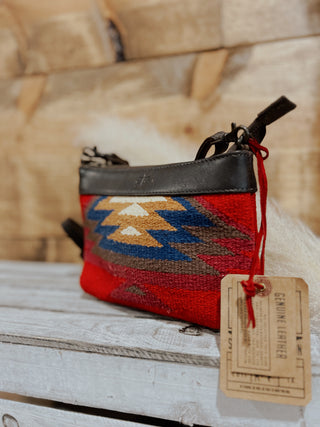 Handbag with a patterned design on a wooden surface, accompanied by a tag.
