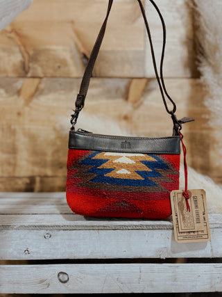 Red and black patterned handbag with a tag on a wooden surface