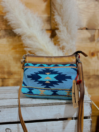 Blue patterned handbag with brown strap on a wooden surface