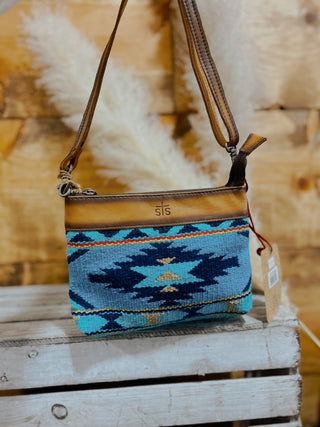 Blue patterned handbag with brown leather strap on a wooden surface