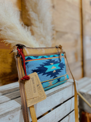 Blue patterned bag with a brown strap on a wooden surface