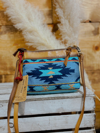 Blue patterned handbag with brown leather straps on a wooden surface