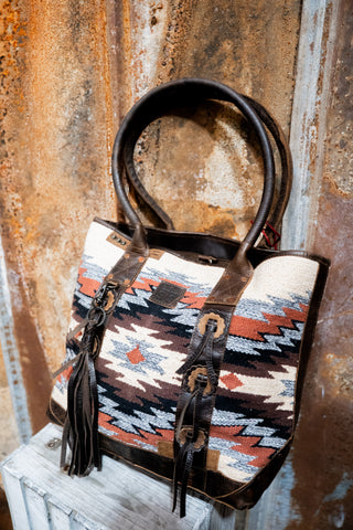 Handbag with tribal pattern and leather straps on a rustic metal surface