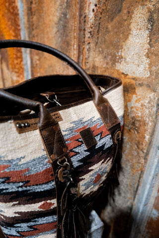 Handbag with patterned fabric and leather accents against a textured wall.